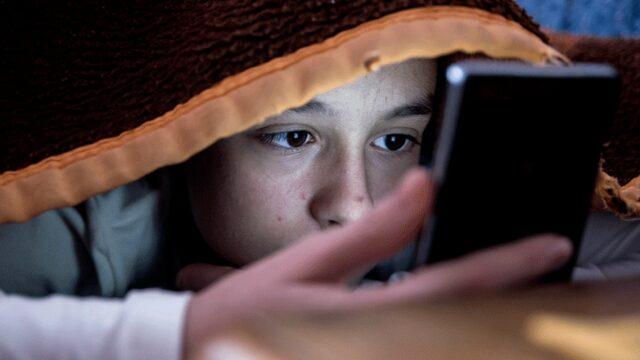 Boy looking at phone under cover