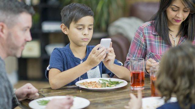 A boy on his phone at the dinner table