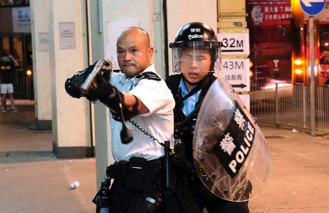 Hong Kong'da bir polis, Çin'e suçlu iade yasa tasarısını protesto eden göstericilere silahını doğrulturken. Fotoğraf, onlarca protestocunun gözaltında tutulduğu Kwai Çung karakolunun önünde çekildi.