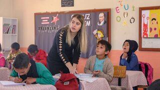 Elif öğretmen, okuma yazma öğrettiği çocuklar ve anneleriyle kitap okuyor