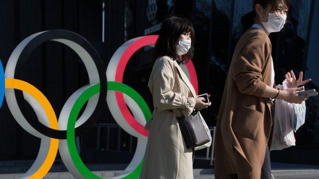 People wearing face masks walk by the Olympic Rings in Tokyo