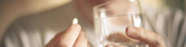 A woman holds a painkiller pill and a glass of water