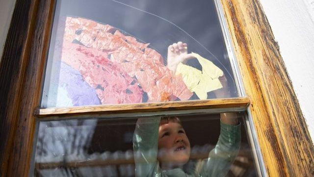 A five-year-old girl sticks a rainbow made of colourful pieces of paper to a window in Munich, Bavaria