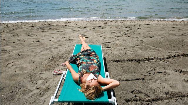 A woman wearing a face mask sunbathes at the beach after it officially reopened for the first time following the country