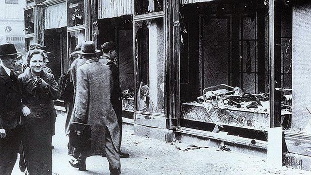 Kristallnacht'tan sonra, vitrin camları kırılmış, Yahudilere ait bir dükkana bakanlar.