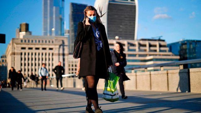 A woman wearing a protective face mask speaks on the phone as she crosses London Bridge