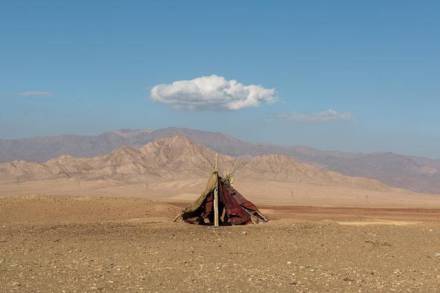 Tent in front of mountains, below a small white cloud in the sky