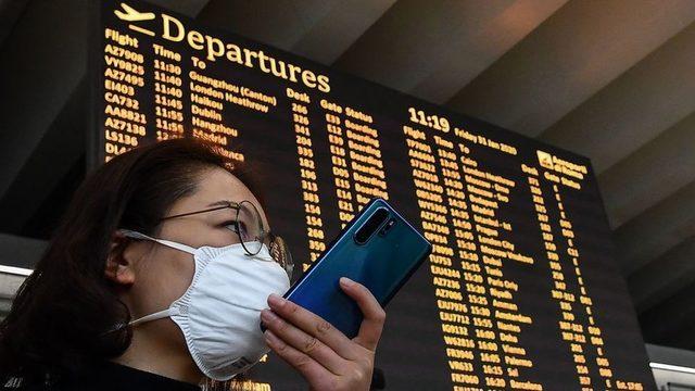 A passenger wearing a respiratory mask speaks on her smartphone by the departures board on January 31, 2020 at Rome's Fiumicino airport