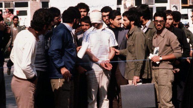 İranlı öğrenciler arasında elleri bağlı halde görülen bir Amerikalı diplomat.