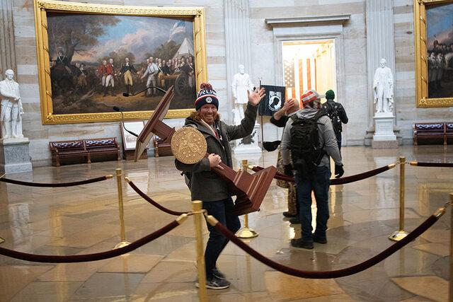Donald Trump destekçisi bir protestocu, 6 Ocak'taki kongre baskınında ABD Temsilciler Meclisi Başkanı Nancy Pelosi'nin kürsüsünü taşıyor. Kongre'nin Joe Biden'ın seçim zaferini onaylamasının hemen ardından, büyük bir kalabalık camları ve kapıları kırarak Kongre binasına girmişti.