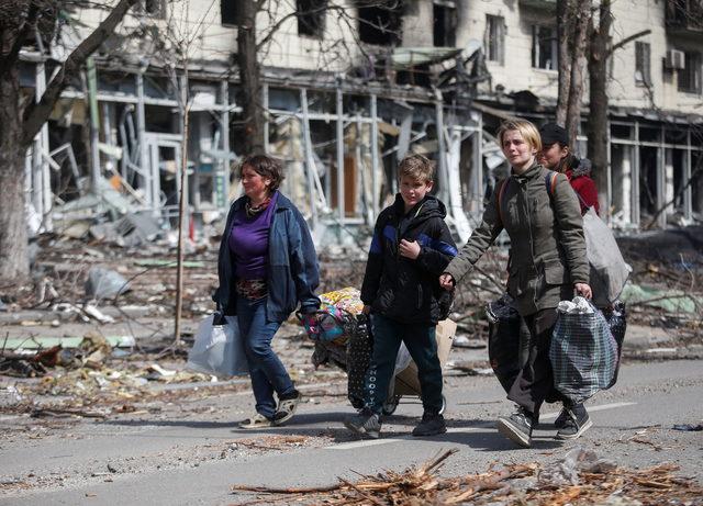 Residents carry their belongings along a street near a building burnt in the course of the Ukraine-Russia conflict, in Mariupol