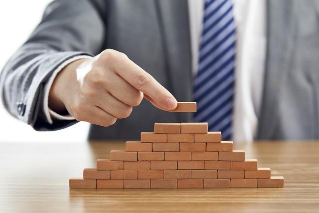 businessman-suit-putting-last-piece-pyramid-using-wooden-blocks_181624-47103