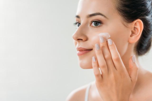 stock-photo-beautiful-smiling-young-woman-applying-face-cream-looking-away