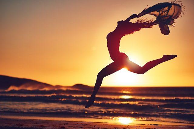 woman on the beach at sunset, jumping about with a sarong flapping in the wind