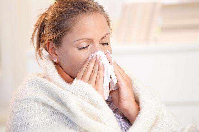 Young woman having flu, feeling bad, blowing her nose, wrapped up in blanket.